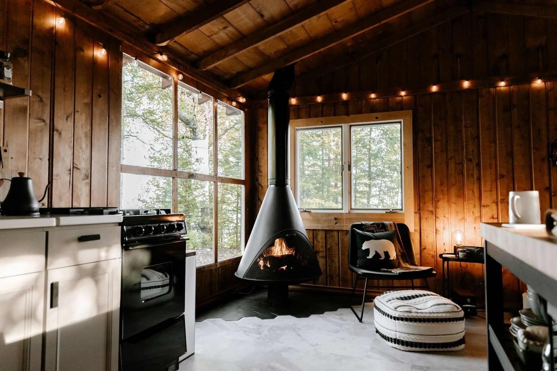A wooden cabin interior with a hanging stove and fairy lights